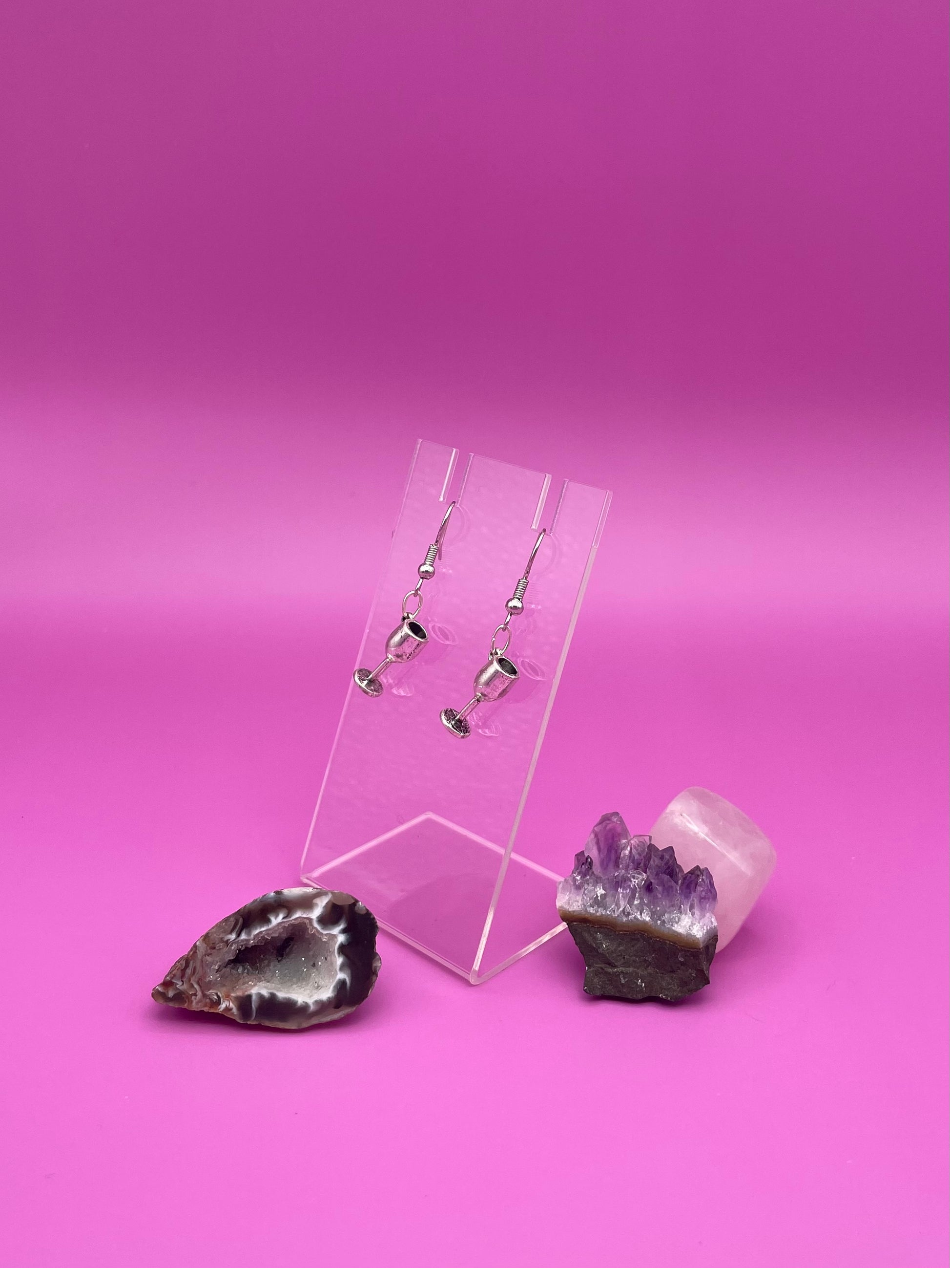 Silver wine glass earrings on a clear stand with purple background