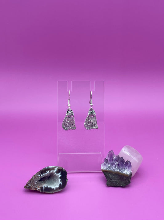 Silver cat earrings on a clear stand with purple background