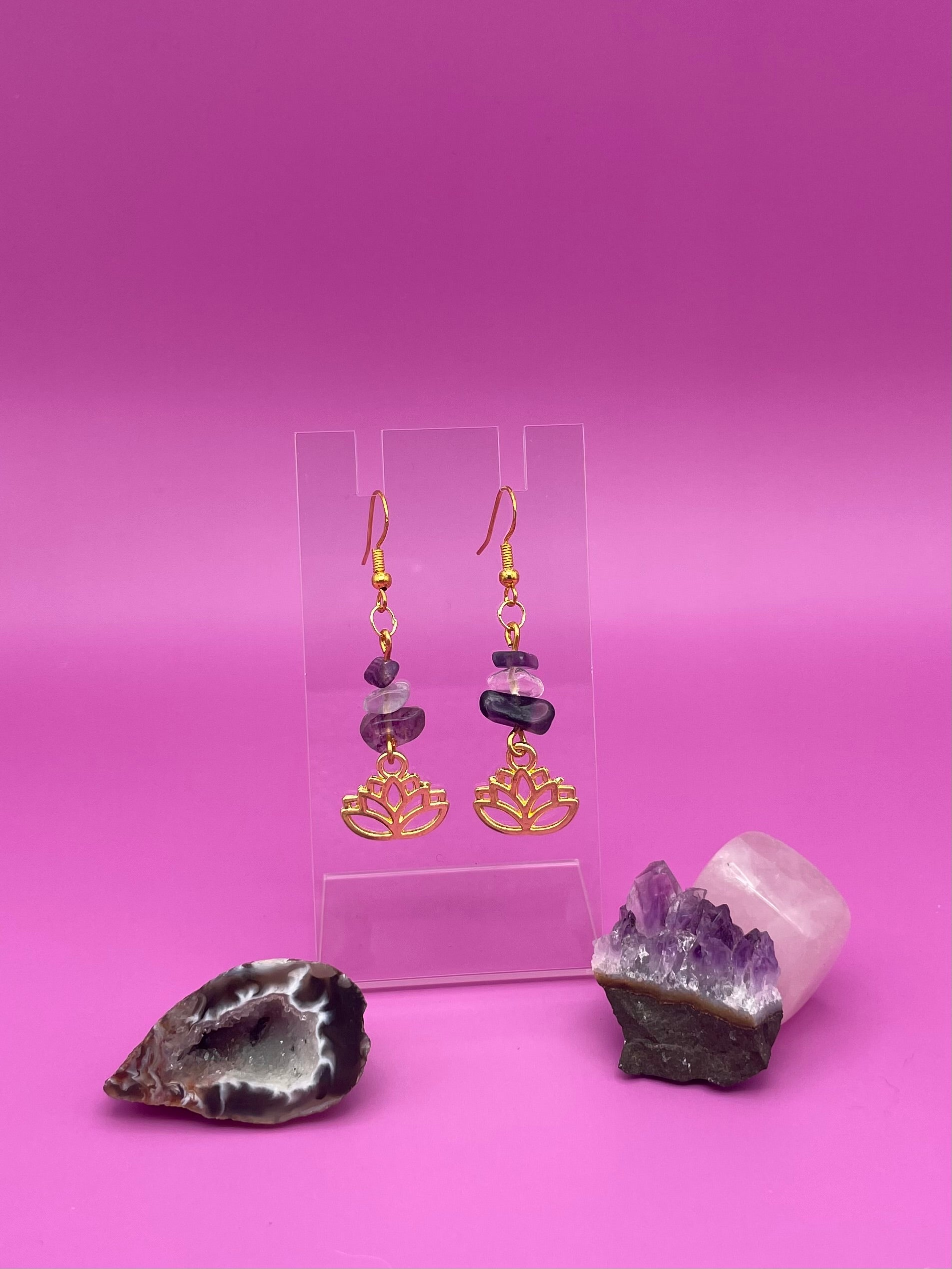Gold lotus flower earrings with fluorite and clear quartz crystal chips on a clear stand with purple background