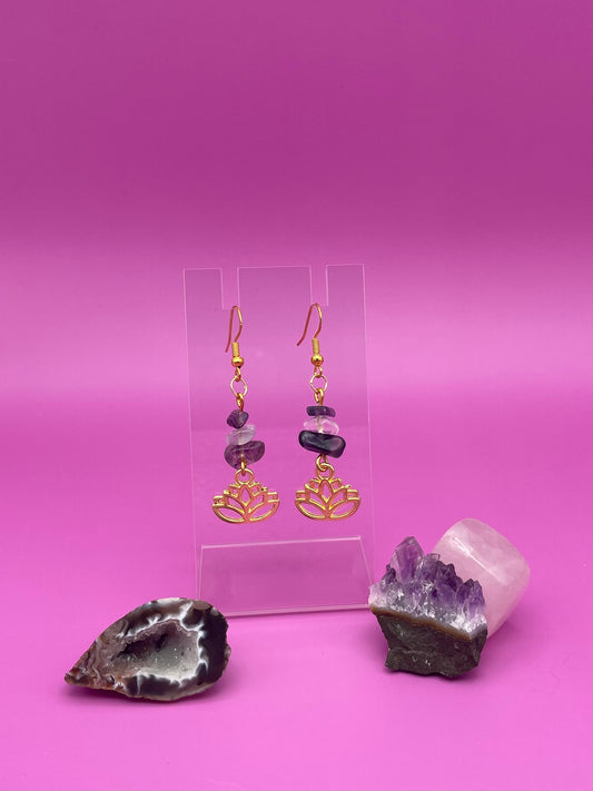 Gold lotus flower earrings with fluorite and clear quartz crystal chips on a clear stand with purple background