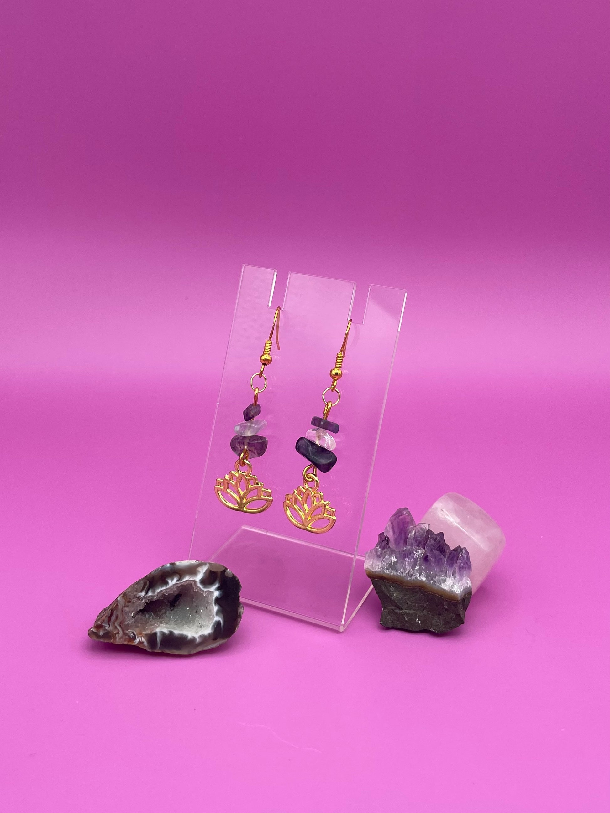 Gold lotus flower earrings with fluorite and clear quartz crystal chips on a clear stand with purple background
