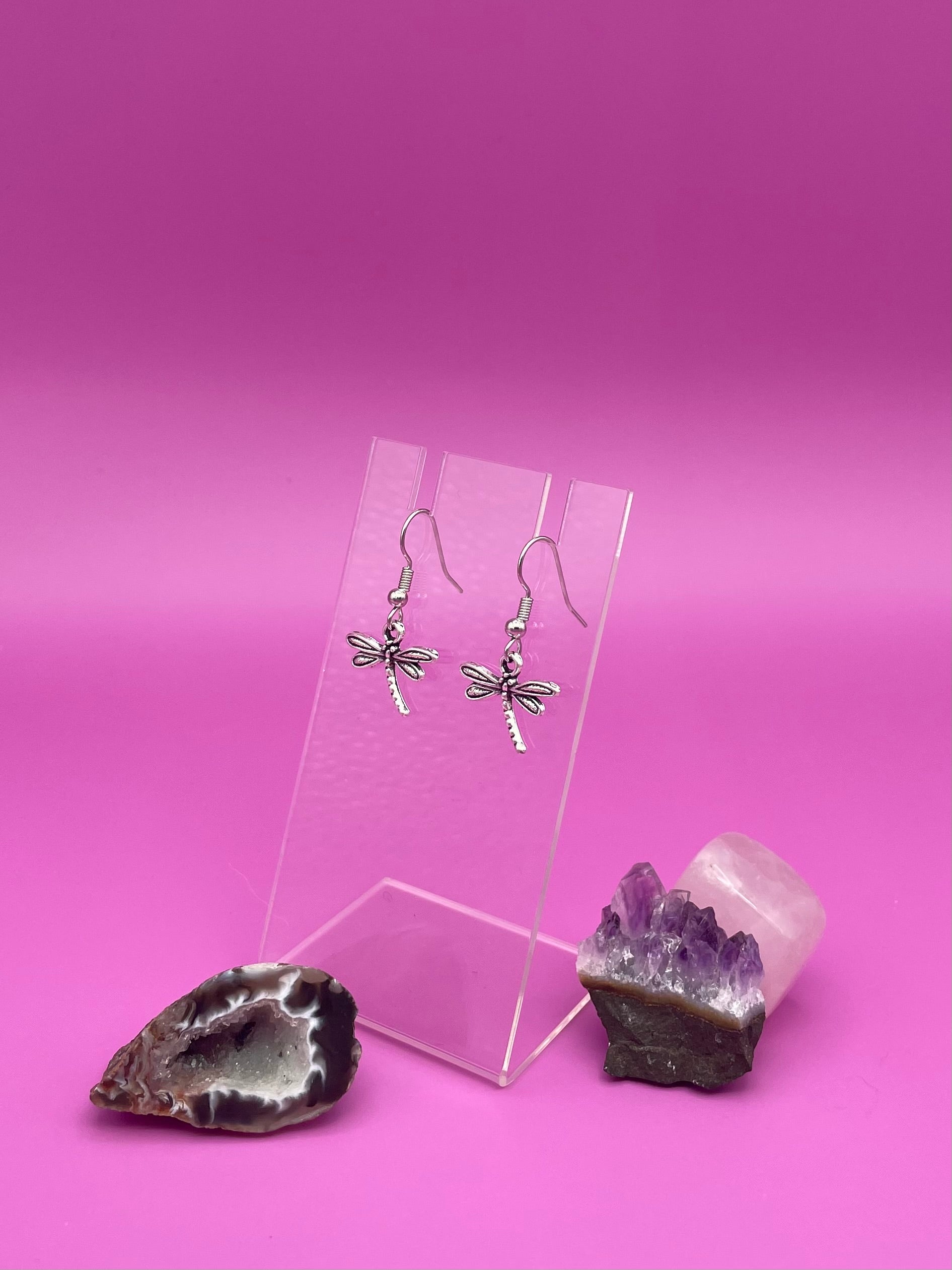 Dragonfly-shaped silver earrings on a clear stand with purple background