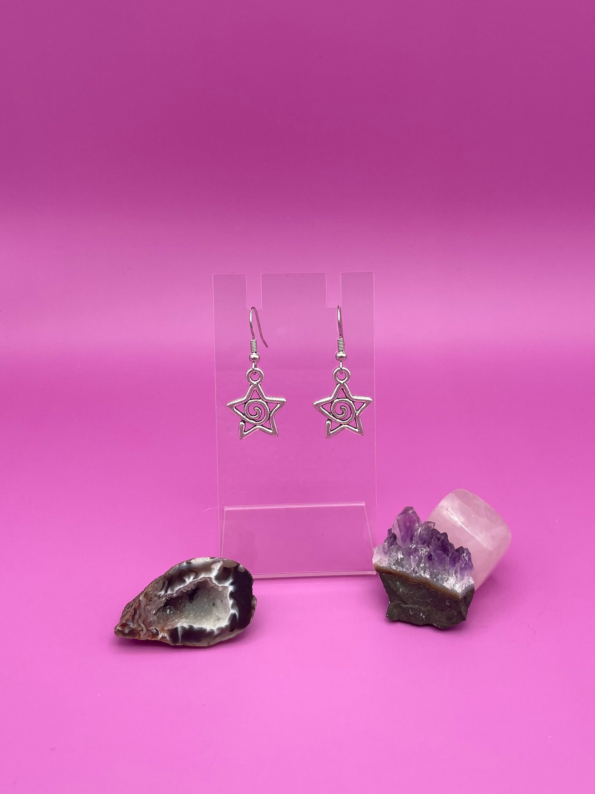 Silver Star-shaped swirl earrings on a clear stand with purple background