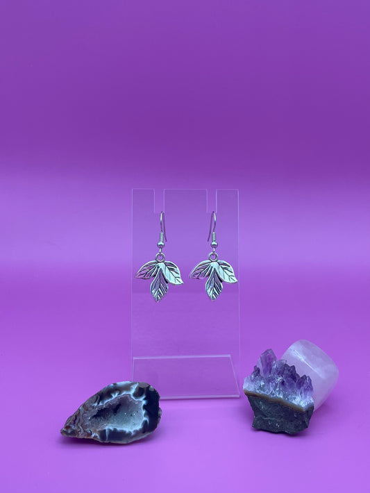 Silver leaf earrings on a clear stand with purple background