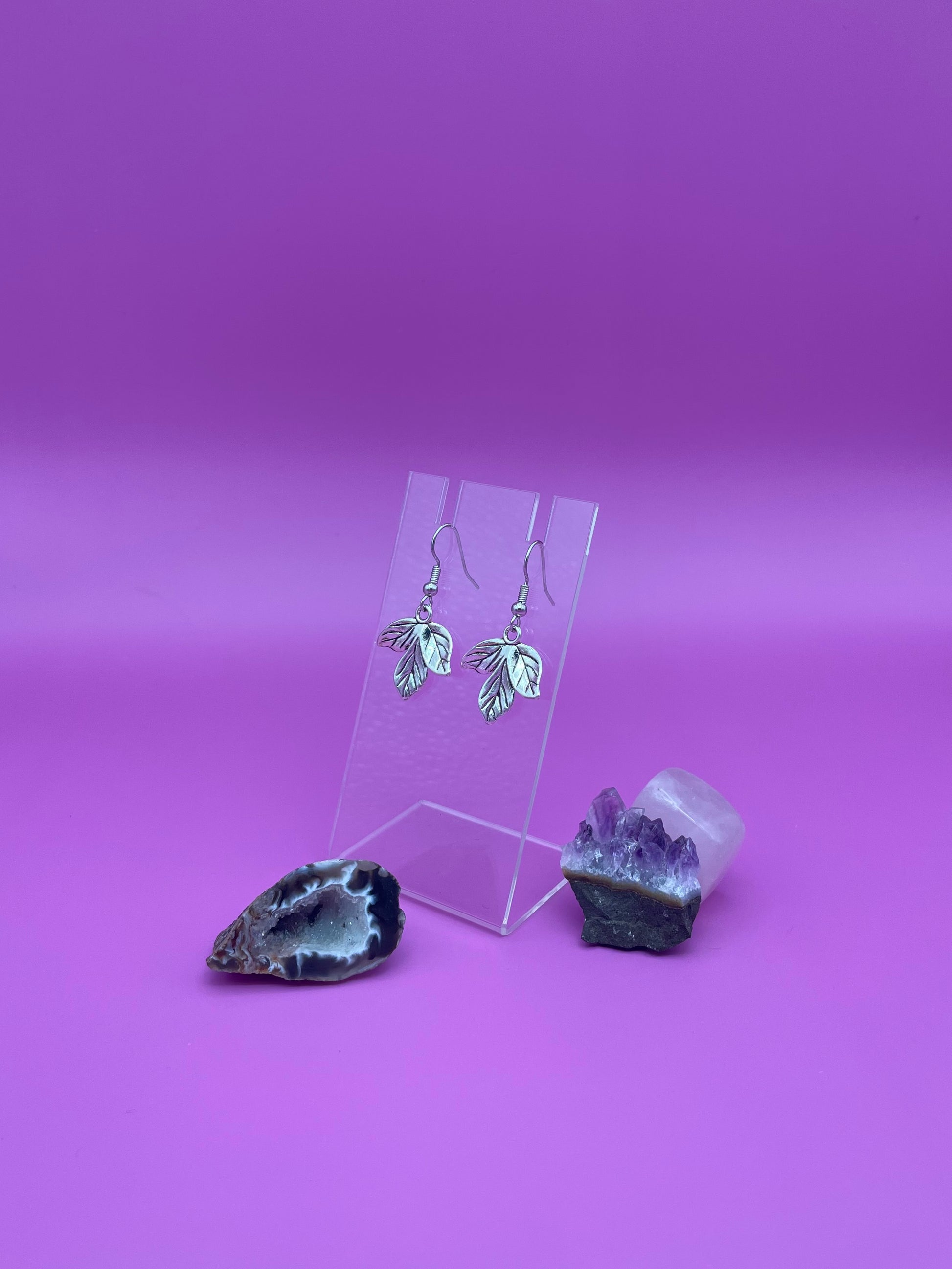 Silver leaf earrings on a clear stand with purple background