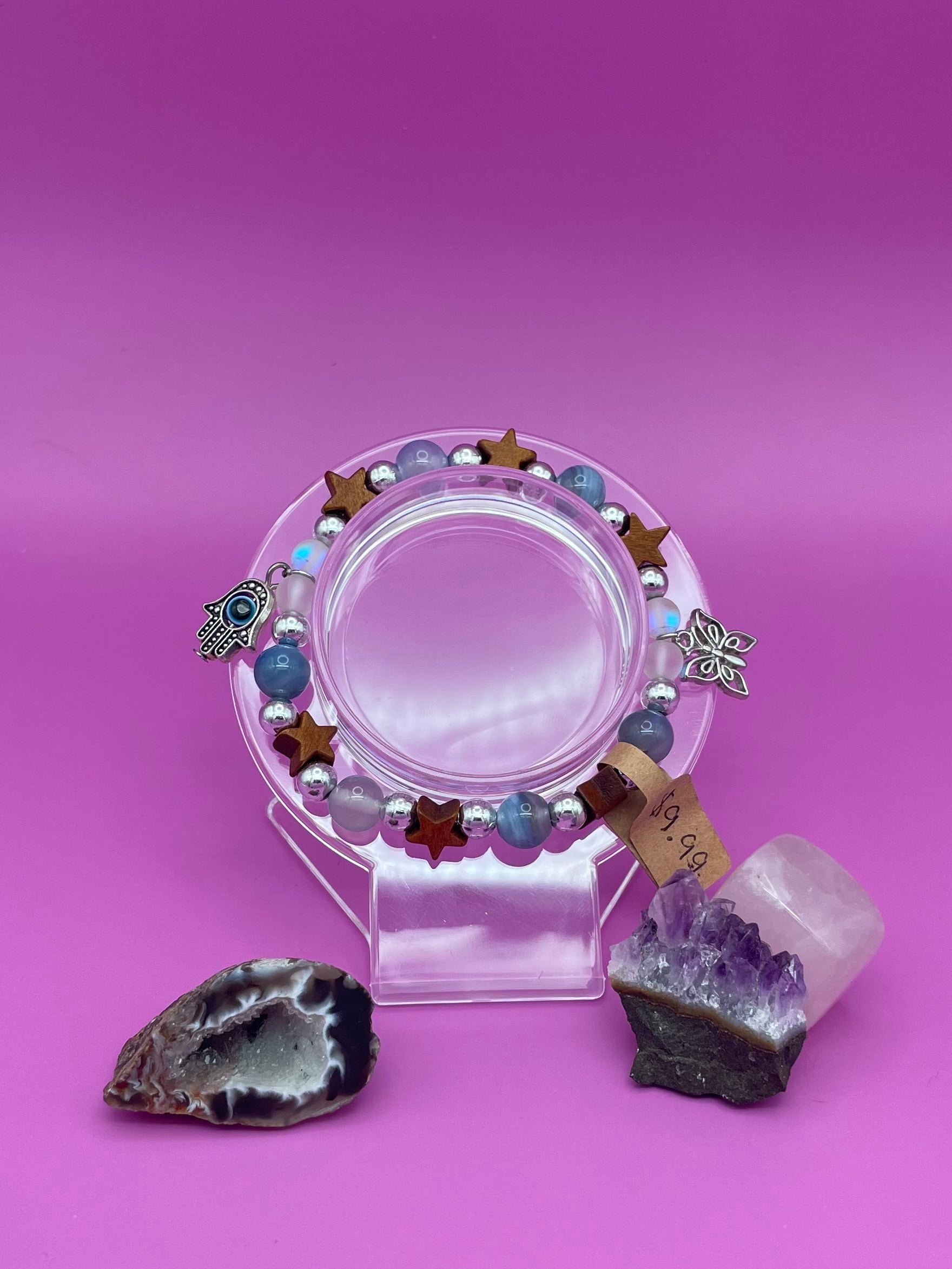 Bracelet with blue lace agate, wooden stars, and aura beads as well as two charms hanging on sides. A butterfly and an evil eye pendant, both silver.