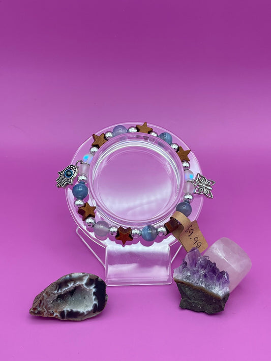 Bracelet with blue lace agate, wooden stars, and aura beads as well as two charms hanging on sides. A butterfly and an evil eye pendant, both silver.