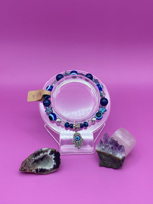 Bracelet with blue beads and Hamsa hand charm on a clear stand with crystals on a purple background