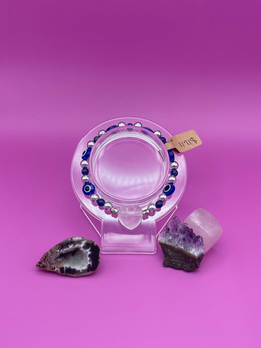 Blue and silver evil eye bracelet with clear quartz crystal centerpiece on clear stand 