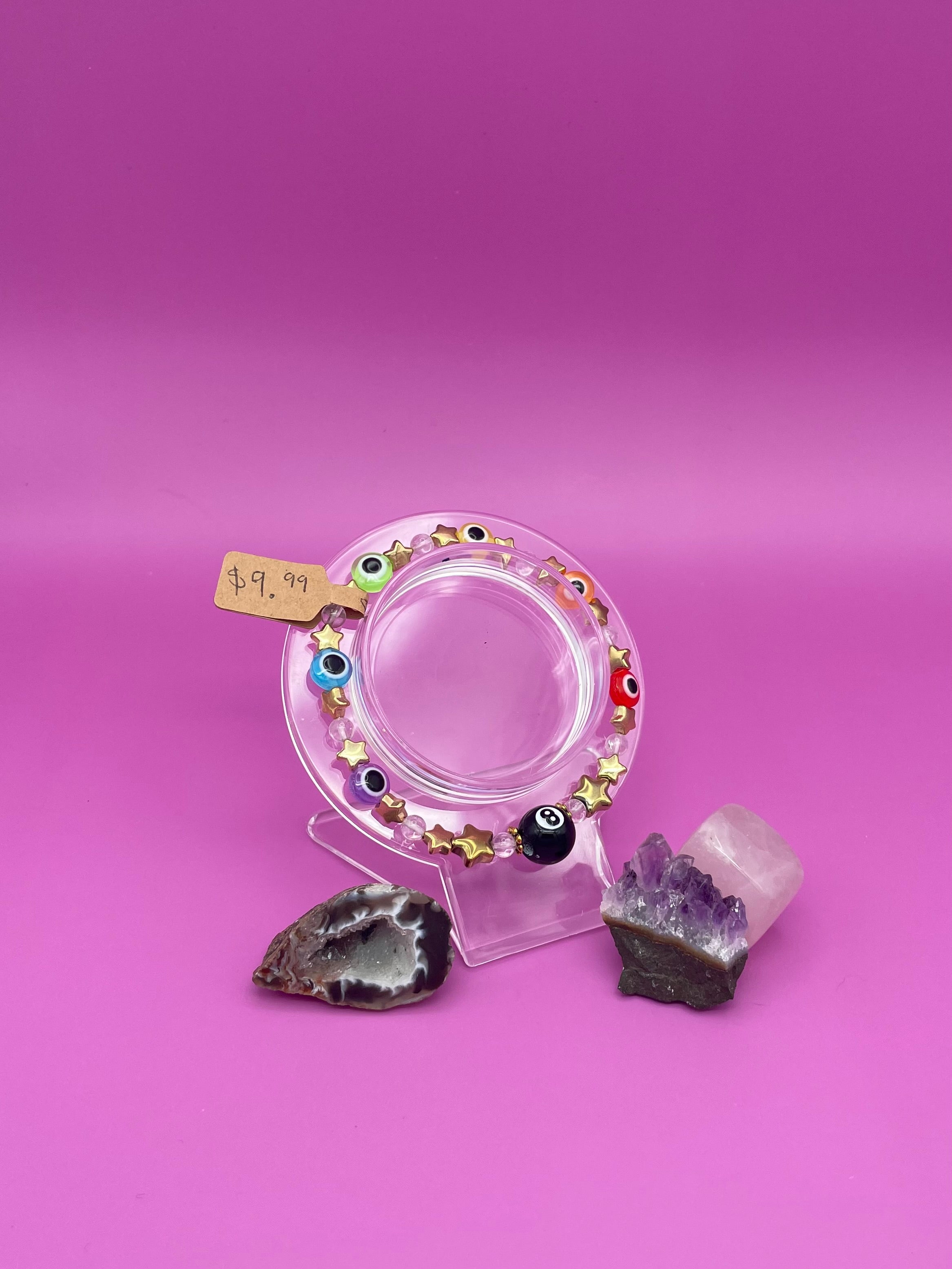 Bracelet with evil eye rainbow beads, gold stars, and clear quartz beads in a pattern with a black 8ball as the main center piece