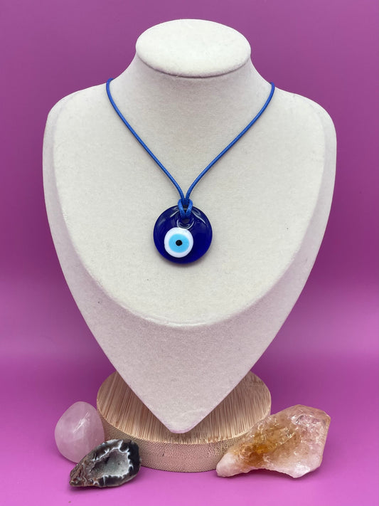 Blue glass evil eye pendant necklace with blue cord on a white mannequin bust against a purple background